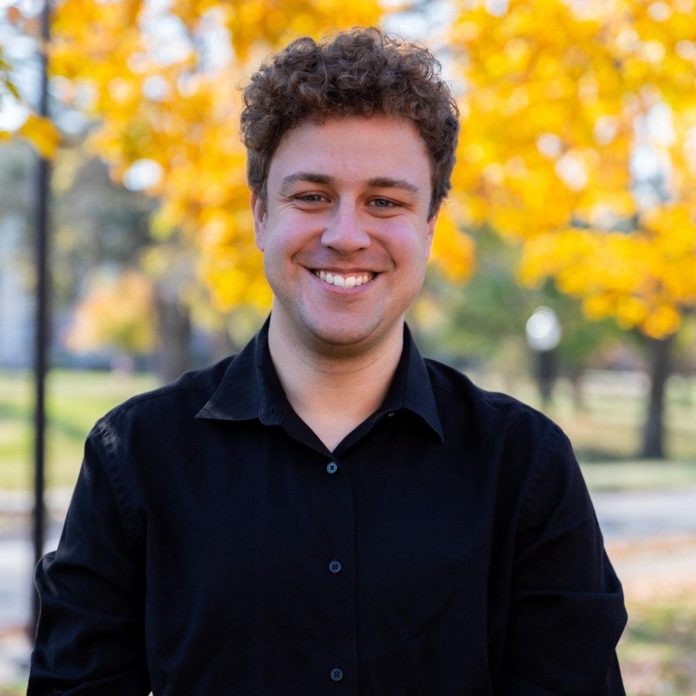 Eric Matherly headshot man with brown hair in black sweater standing in front of yellow tree in fall